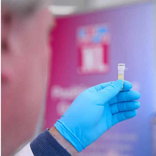 Een laborant met blauwe handschoen houdt een buisje met ingestuurd testmateriaal omhoog