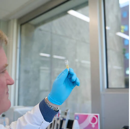 Laborant met blauwe handschoenen beoordeelt een buisje met testmateriaal in het laboratorium