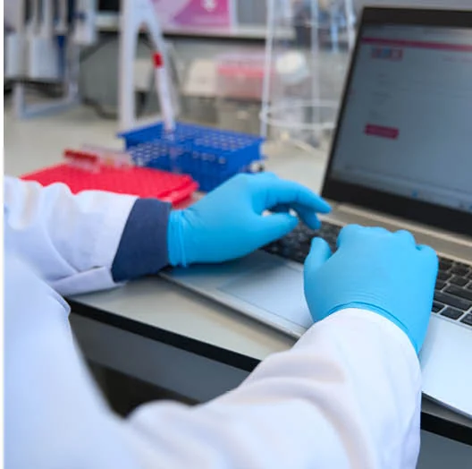 Laborant met handschoenen verwerkt testgegevens op een laptop in het laboratorium