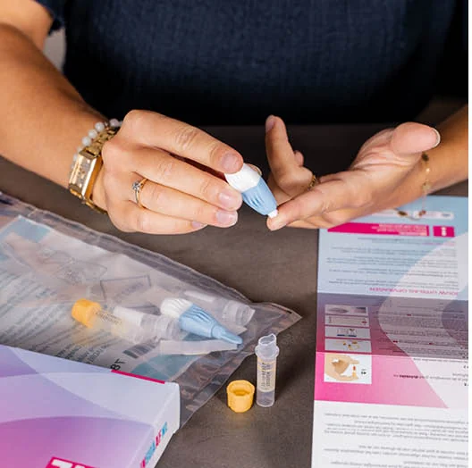 Vrouw maakt het prikpennetje van de thuistest klaar, met de buisjes en de verzendzak op tafel